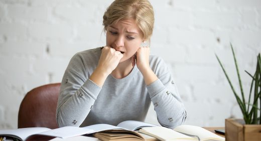 Portrait of a student girl sitting at the desk biting her fist